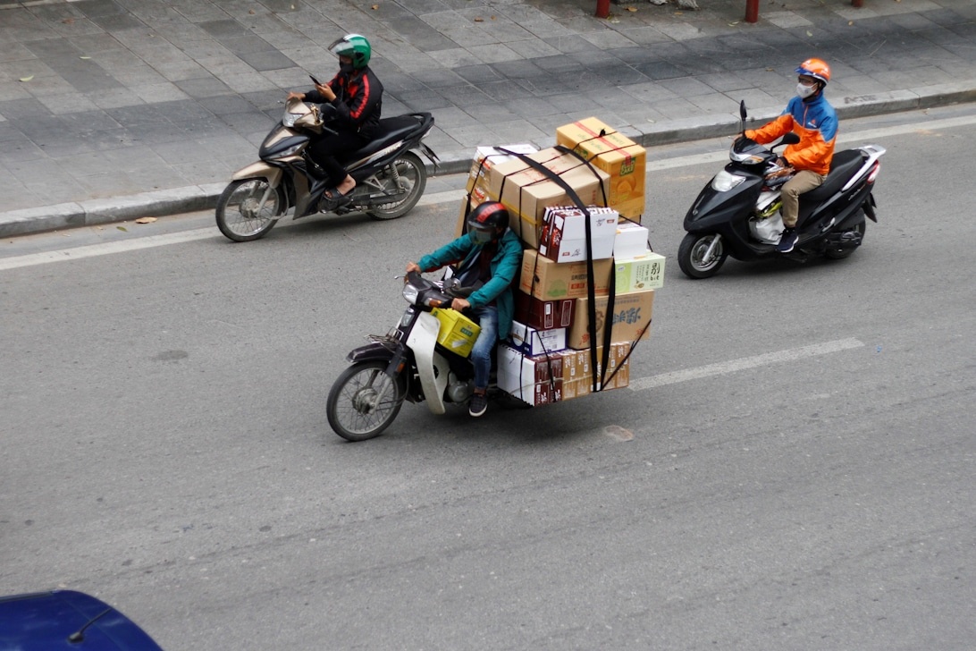 Ein Motorrad-Lieferfahrer im Verkehr mit einem großen Stapel Pakete, was kostengünstige Kleinunternehmenslogistik und Last-Mile-Lieferlösungen demonstriert.
