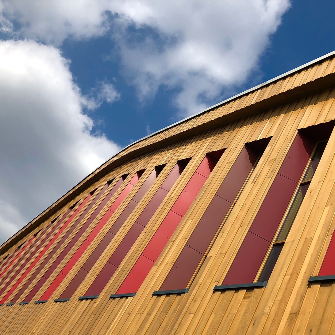 Ein modernes architektonisches Gebäude mit umfangreicher Naturholzverkleidung, geschwungener Dachlinie und roten Akzentpaneelen.