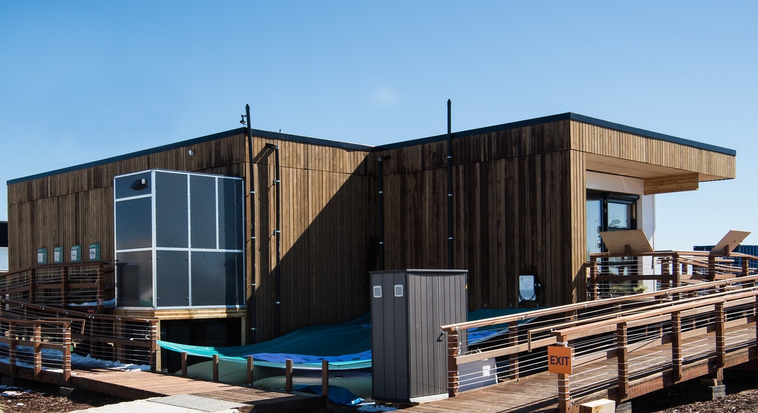 Ein modernes, nachhaltiges Haus mit dunkler Holzverkleidung, großen Fenstern und einer Holzterrasse.